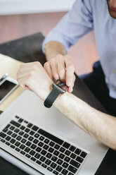 Junger Geschäftsmann arbeitet im Büro und schaut auf seine Smartwatch - GIOF03250