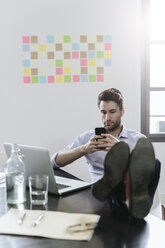 Young businessman working in office, using smartphone - GIOF03258