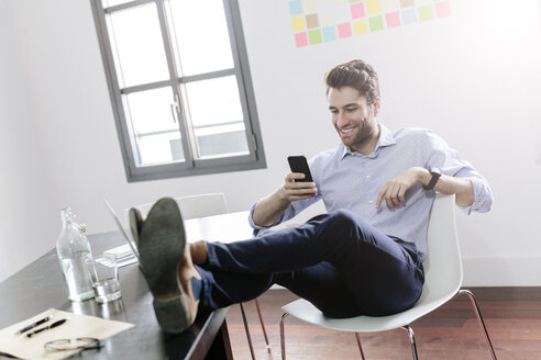 Junger Geschäftsmann arbeitet im Büro und benutzt sein Smartphone - GIOF03259