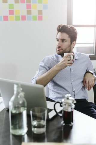 Junger Geschäftsmann sitzt am Schreibtisch mit einer Kanne Kaffee, lizenzfreies Stockfoto