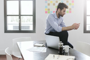 Young businessman working in office, using smartphone - GIOF03265