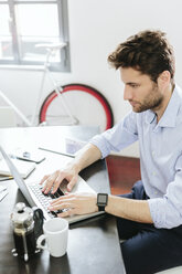 Young businessman working in office, using laptop - GIOF03268