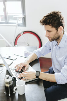 Junger Geschäftsmann bei der Arbeit im Büro, mit Laptop - GIOF03268