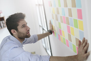 Young businessman working in office with sticky notes on wall - GIOF03282