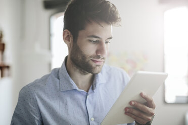 Junger Geschäftsmann arbeitet im Büro und schaut auf ein digitales Tablet - GIOF03287