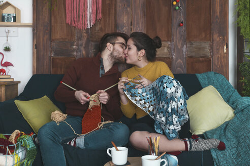 Young couple doing needleworks kissing on the couch - RTBF01008