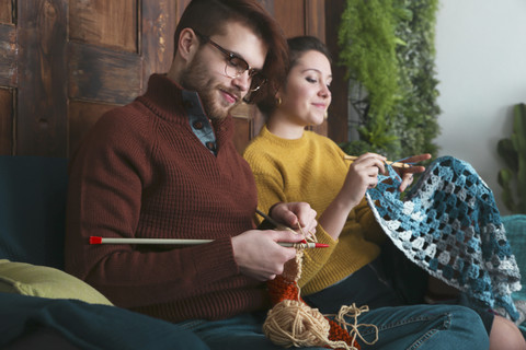 Junges Paar strickt und häkelt im Wohnzimmer, lizenzfreies Stockfoto