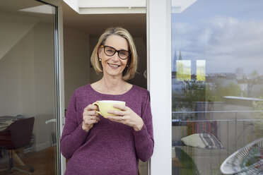 Porträt einer lächelnden reifen Frau mit Kaffeetasse auf dem Balkon - RBF06033