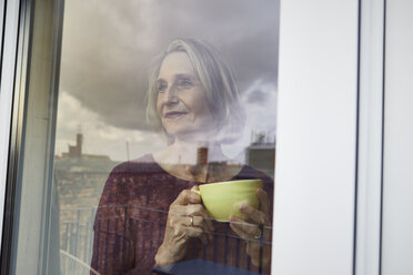 Ältere Frau hält Kaffeetasse und schaut aus dem Fenster - RBF06034