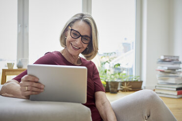 Lächelnde reife Frau zu Hause mit Tablet auf dem Sofa - RBF06036