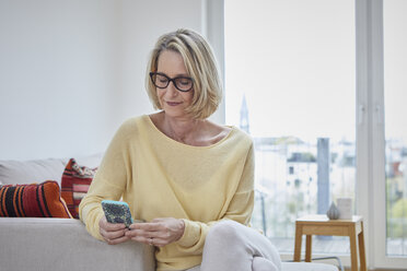 Reife Frau zu Hause mit Blick auf das Handy auf dem Sofa - RBF06038