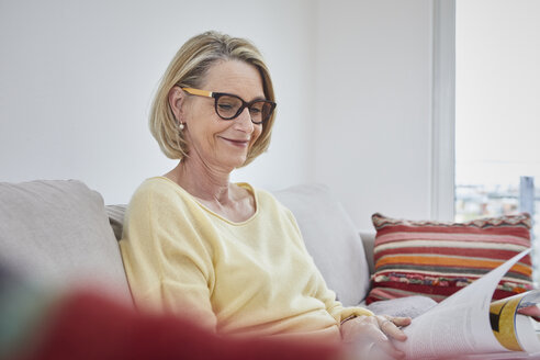 Lächelnde reife Frau zu Hause auf dem Sofa beim Lesen einer Zeitschrift - RBF06041