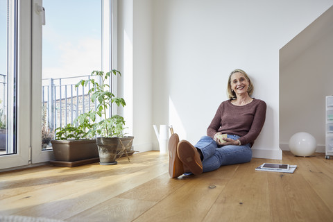 Porträt einer lächelnden reifen Frau, die zu Hause auf dem Boden sitzt, lizenzfreies Stockfoto