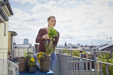 Lächelnde reife Frau, die sich um Pflanzen auf dem Balkon kümmert - RBF06052