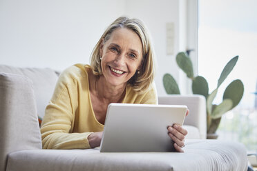 Lächelnde reife Frau zu Hause mit Tablet auf dem Sofa - RBF06059