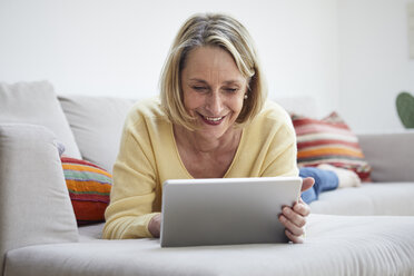 Lächelnde reife Frau zu Hause mit Tablet auf dem Sofa - RBF06060