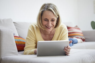 Smiling mature woman at home using tablet on the sofa - RBF06060