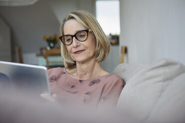 Mature woman at home using tablet on the sofa - RBF06063