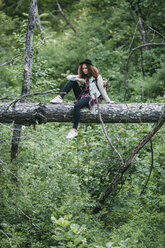 Teenage girl with camera sitting on deadwood in nature - VPIF00098