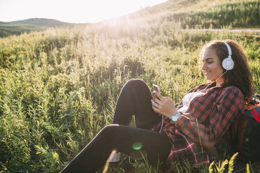 Teenage girl listening music with headphones on a meadow looking at cell phone - VPIF00117