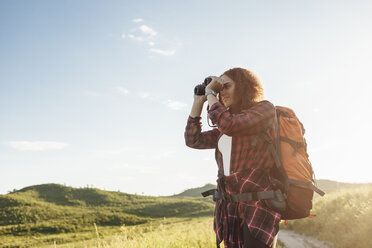 Teenage girl with backpack using binoculars in nature - VPIF00131
