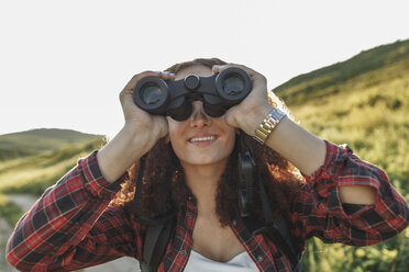 Teenage girl with backpack using binoculars in nature - VPIF00133