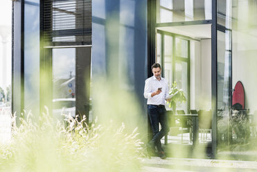 Geschäftsmann vor einem Bürogebäude mit Blick auf ein Mobiltelefon - UUF11684