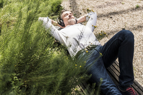 Businessman with headphones lying on a bench - UUF11686