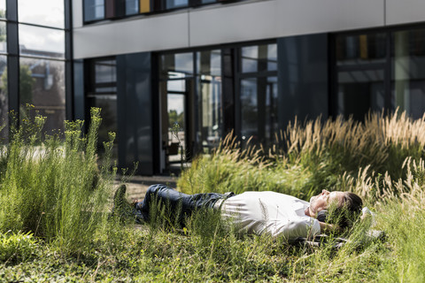 Geschäftsmann mit Kopfhörern auf einer Bank vor einem Bürogebäude liegend, lizenzfreies Stockfoto