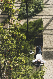 Businessman with headphones lying on a bench next to tablet - UUF11694