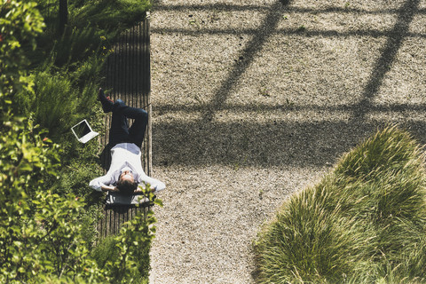 Geschäftsmann mit Kopfhörern auf einer Bank neben einem Tablet liegend, lizenzfreies Stockfoto