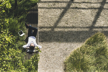 Businessman with headphones lying on a bench next to tablet - UUF11695