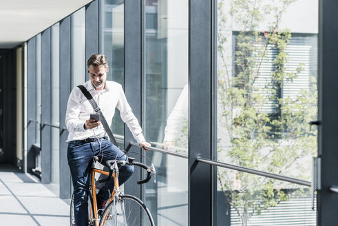 Geschäftsmann mit Handy auf dem Fahrrad in einer Büropassage - UUF11699