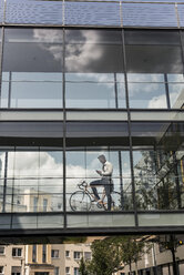 Geschäftsmann mit Mobiltelefon und Fahrrad in einem Bürogang - UUF11701