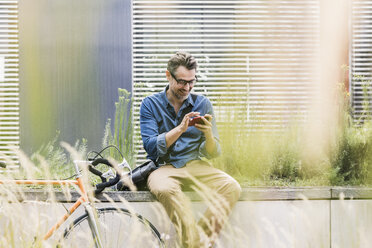 Smiling businessman using cell phone next to bicycle - UUF11725