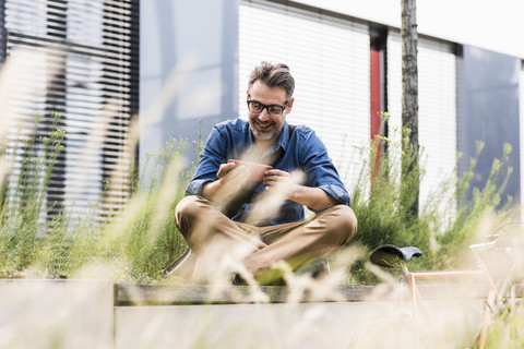 Smiling businessman using cell phone next to bicycle stock photo