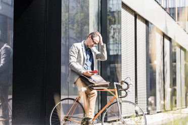 Shocked businessman on bicycle looking at cell phone - UUF11728