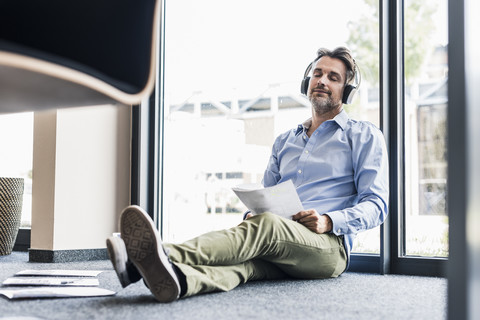 Geschäftsmann mit Kopfhörern sitzt auf dem Boden im Büro, lizenzfreies Stockfoto