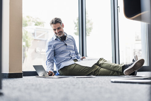 Lächelnder Geschäftsmann bei der Arbeit auf dem Boden im Büro - UUF11732