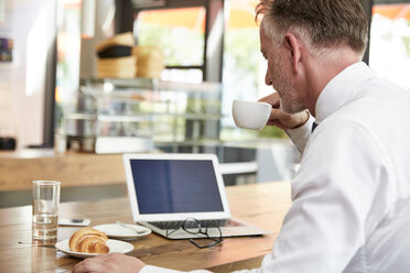 Businessman having breakfast at the airport, using laptop - SUF00320