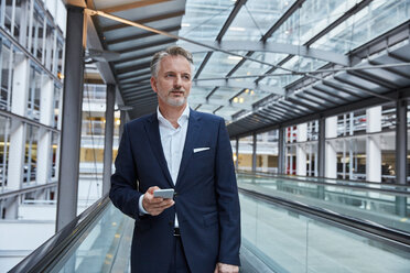 Businessman using smartphone at the airport, standing on moving walkway - SUF00336