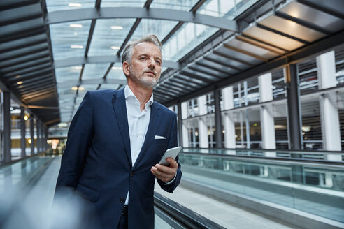 Businessman using smartphone at the airport, standing on moving walkway - SUF00337