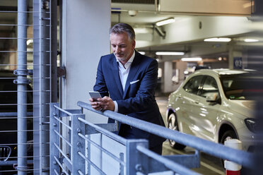 Businessman using smartphone in parking garage - SUF00338