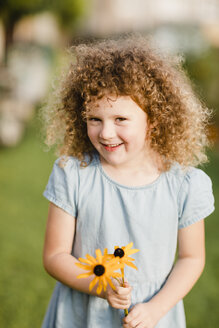 Porträt eines glücklichen kleinen Mädchens mit gepflückten Blumen im Garten - NMSF00164