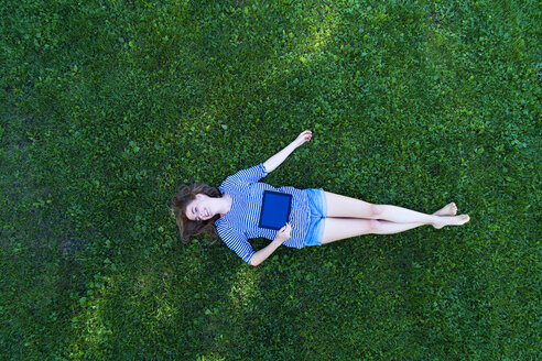 Young woman lying on grass, holding digital tablet - MAEF12416