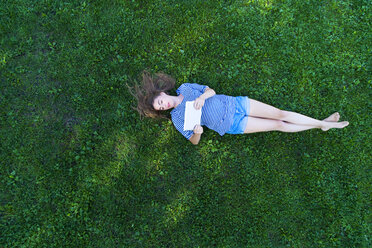 Young woman lying on grass, holding digital tablet - MAEF12418