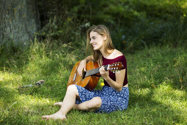 Junge Frau sitzt auf einer Wiese und spielt Gitarre - MAEF12425