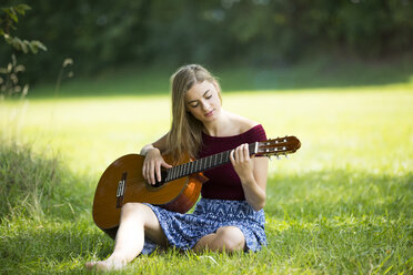 Junge Frau sitzt auf einer Wiese und spielt Gitarre - MAEF12426