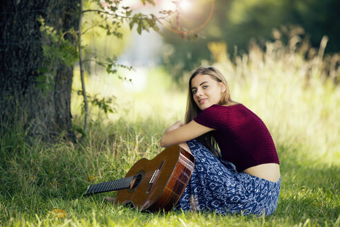 Junge Frau sitzt auf einer Wiese und spielt Gitarre - MAEF12427