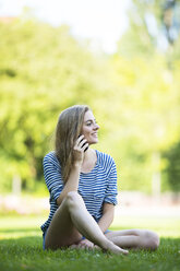 Young woman sitting on grass talking on the phone - MAEF12430